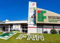Fachada do IFRN Campus Mossoró, com letreiro do instituto, banner de 20 anos e as letras IFRN no gramado