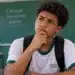 Estudante de escola pública com expressão pensativa e mão apoiada no queixo, em sala de aula, ilustrando dúvidas sobre o pagamento do Pé-de-Meia.