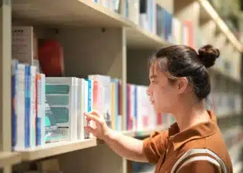 Mulher olha um livro em estante de biblioteca, cena sobre como escrever título de livro com maiúscula ou minúscula