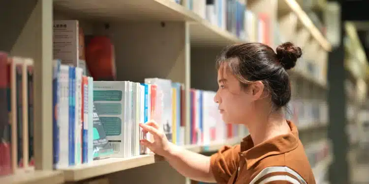 Mulher olha um livro em estante de biblioteca, cena sobre como escrever título de livro com maiúscula ou minúscula