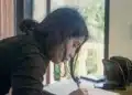 Mulher escreve em caderno sobre a mesa, revisando palavras que perderam o trema com o Acordo Ortográfico