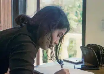 Mulher escreve em caderno sobre a mesa, revisando palavras que perderam o trema com o Acordo Ortográfico
