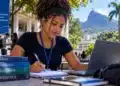 Universitária com cabelo cacheado estuda com notebook e livros de ciência, tecnologia, engenharia e matemática em ambiente acadêmico no Rio de Janeiro.